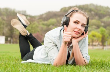 Neşeli kadın çimenlerin üzerinde yatan ve açık havada başparmak gösteren