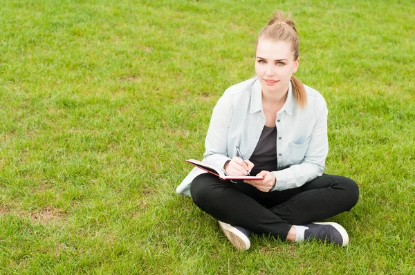 Mulher sorridente bonita sentada na grama com notebook — Fotografia de Stock