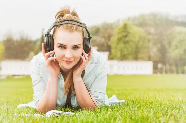 Doğada okuyan, gülümseyen ve müzik dinleyen güzel kız — Stok fotoğraf