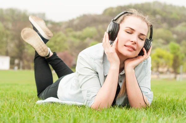 Beautiful girl in park wearing headphones and resting on grass — Stock Photo, Image