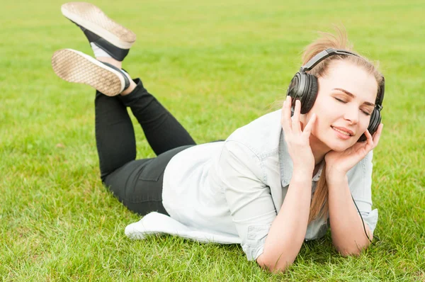 Young woman lying on grass and listen to music — Stok fotoğraf