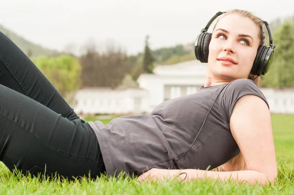 Atraktivní žena sedí venku sluchátka na poslech mu — Stock fotografie
