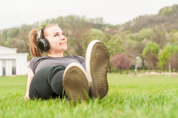 Mutlu kız arkasında yatan ve çimlerin üzerine müzik dinleme — Stok fotoğraf