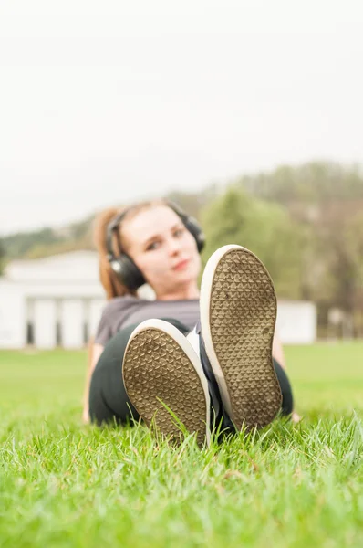 Müzik dinleme genç kadınla çimenlerin üzerinde cross-legged yalan — Stok fotoğraf