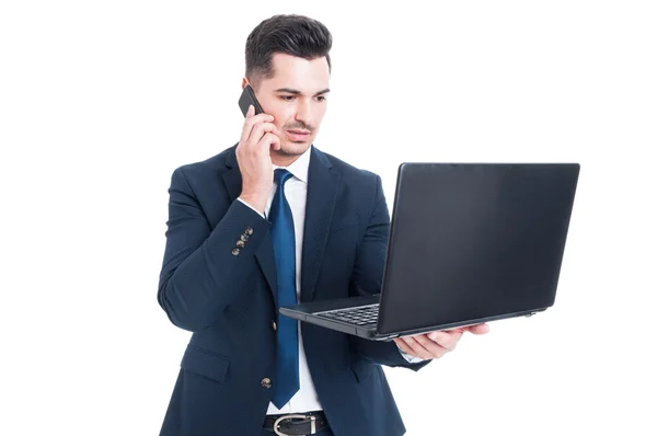 Hombre de negocios guapo hablando en el teléfono inteligente y trabajando en el portátil — Foto de Stock