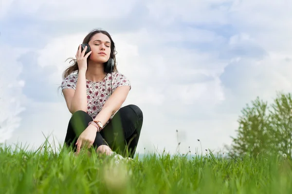 잔디에 앉아 그녀의 머리에 헤드폰 소녀 — 스톡 사진