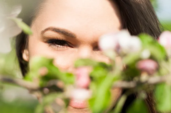 Gros plan de jeune femme attrayante regardant à travers les branches en fleurs — Photo