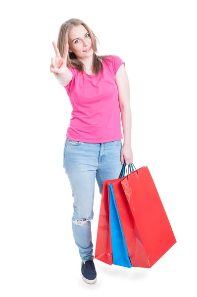 Feliz sorrindo mulher segurando sacos de compras e fazendo gestos de paz — Fotografia de Stock