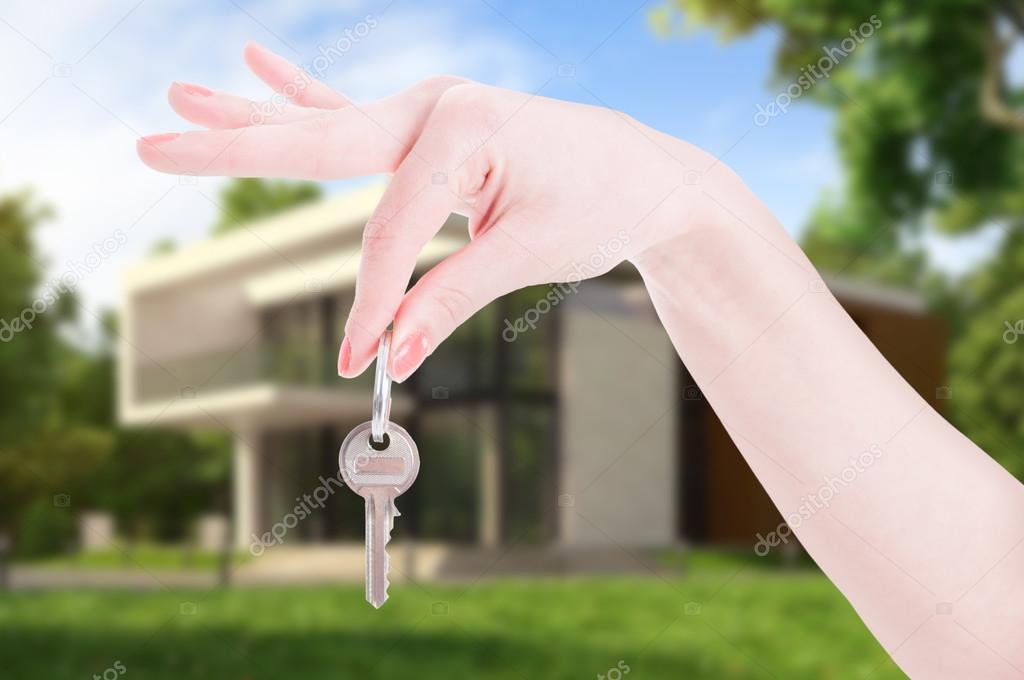 Female hand hanging house key as real estate concept