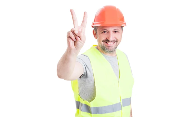 Guapo obrero sonriente o constructor con casco mostrando vict — Foto de Stock