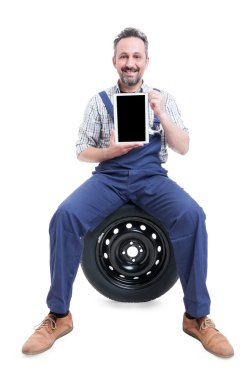 Yakışıklı tamirci lastik üzerinde oturan ve tablet gösteren