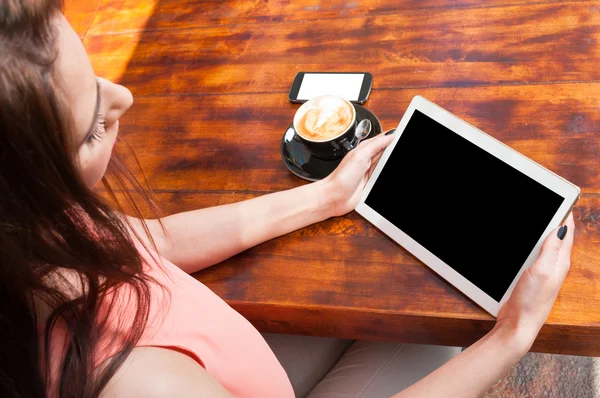 Mujer sosteniendo tableta con café y teléfono inteligente a un lado — Foto de Stock