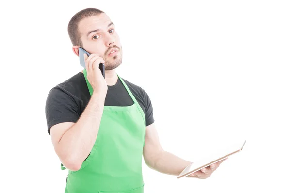 Serious hypermarket clerk talking at phone and holding tablet — Stock Photo, Image