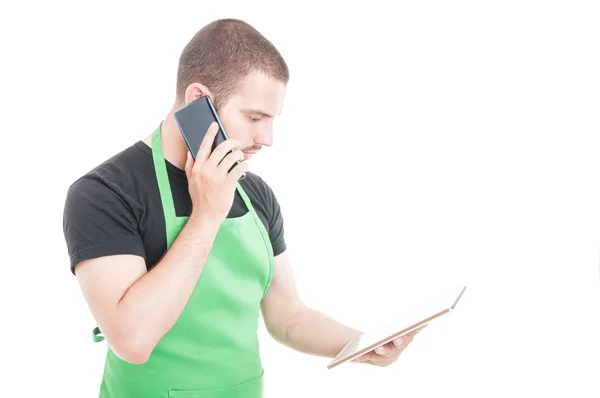 Joven empleado sosteniendo la tableta y hablando por teléfono — Foto de Stock