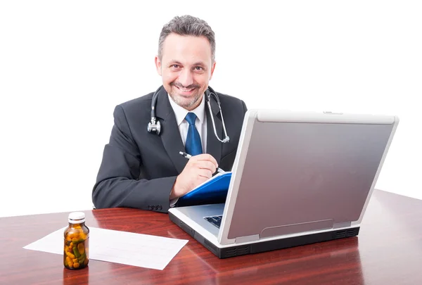 Médecin masculin au bureau souriant et écrivant sur presse-papiers Images De Stock Libres De Droits