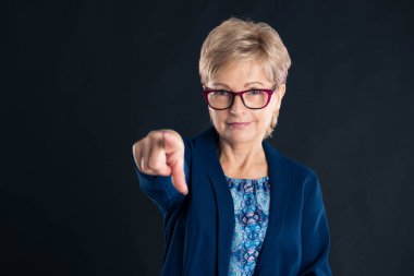 Yaşlı sekreter kamerayı işaret ediyor ve kırmızı gözlük takıyor.