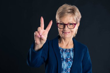 Kırmızı gözlük takan ve kameraya bakıp barış işareti gösteren yaşlı bir sekreterin portresi.