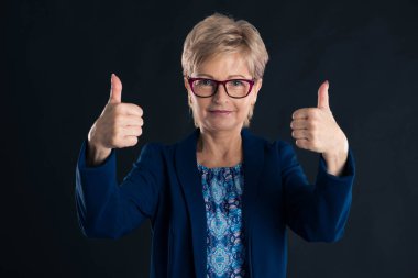 Yaşlı sekreter koyu renk arka planda mor gözlük takıyor.