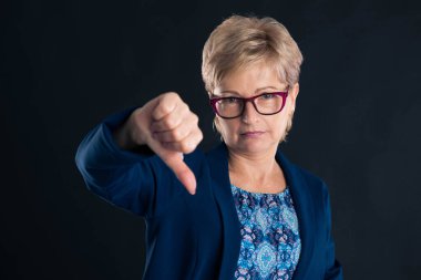 Üzgün yaşlı sekreter koyu arka planda, morumsu gözlük takıyor.