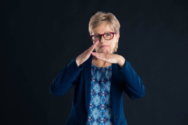 Kıdemli sarışın sekreter koyu bir arkaplan ve mavi ceket giyiyor.