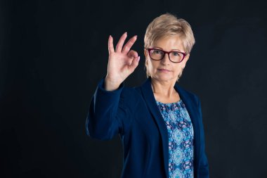 Büyük sekreter her şeyin yolunda olduğunu söylüyor. Koyu bir arka planda mavi bir ceket giyiyorlar.