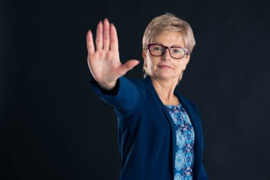 Eflatun gözlük takan yaşlı ve güzel bir sekreter ve koyu arkaplanda dur diyen mavi bir ceket.