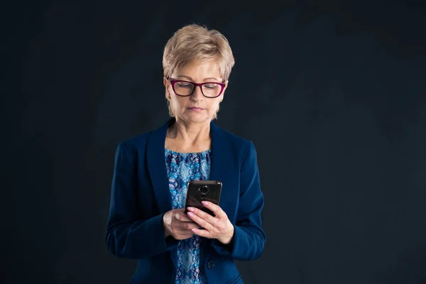 Older businesswoman texting on her mobile phone on a dark background