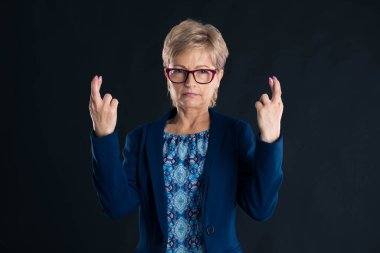 Eski sekreter kötü şans işareti gösteriyor. Koyu bir arka planda mavi bir ceket giyiyor.