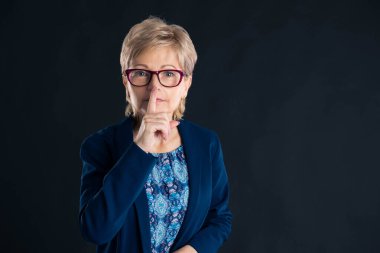 Kıdemli sekreter karanlık bir arka planda sessizlik jesti yapıyor.