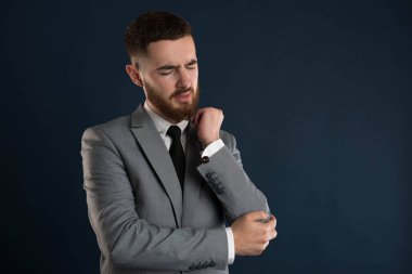 Gri ceketli, dirsek ağrısı olan yakışıklı, beyaz yakalı bir işçi.