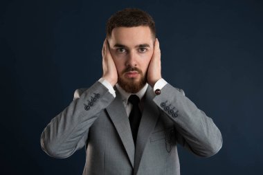 Gri takım elbiseli ve siyah kravatlı elleri kulaklarına kadar uzanan yakışıklı genç bir işadamı.