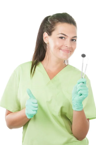 Mujer dentista sosteniendo herramientas profesionales y mostrando pulgares hacia arriba — Foto de Stock