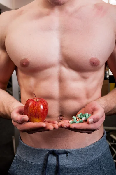 Muscle man choice between apple and pills — Stock Photo, Image