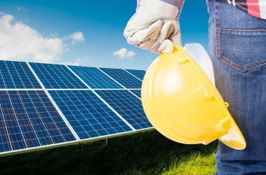 Sarı kask güneş enerjisi panelleri arka planda tutan mühendisi