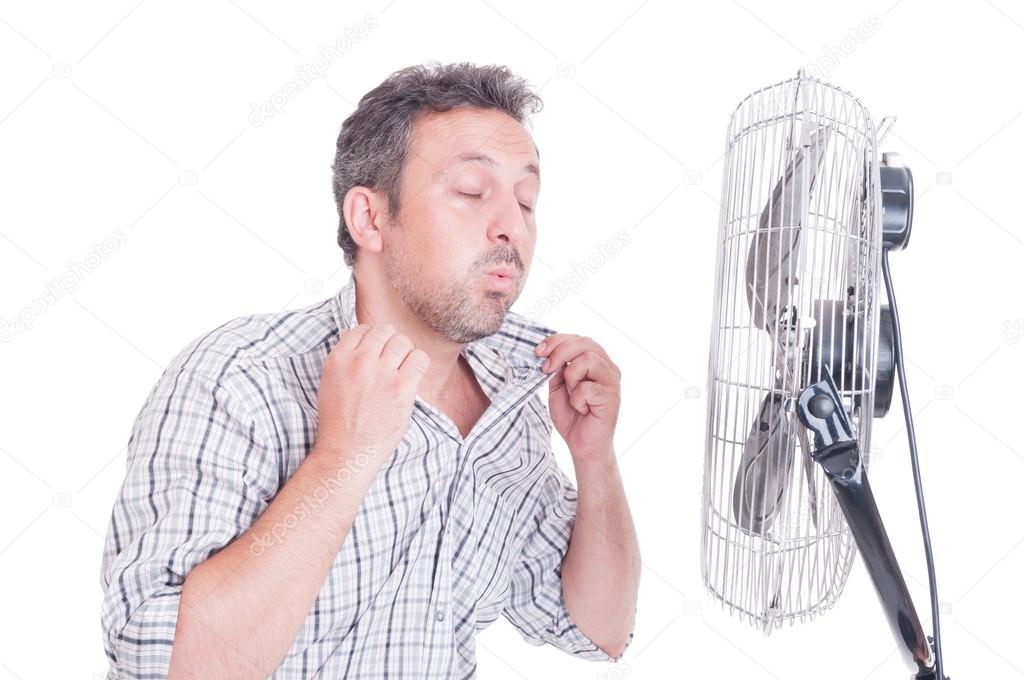 Sweaty man opening shirt in front of cooling fan