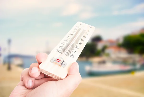 Hand met thermometer op stad met meer achtergrond — Stockfoto