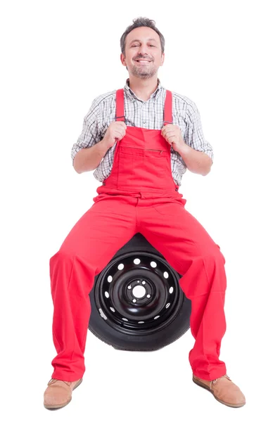 Proud mechanic sitting on car wheel tire — Stock Photo, Image