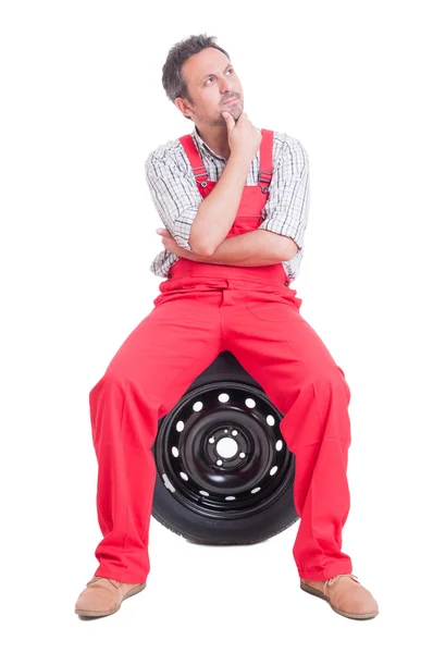 Smart mechanic thinking and sitting on tire — Stock Photo, Image