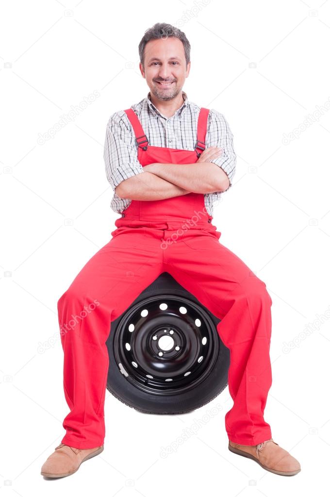 Confident mechanic sitting on car wheel tire