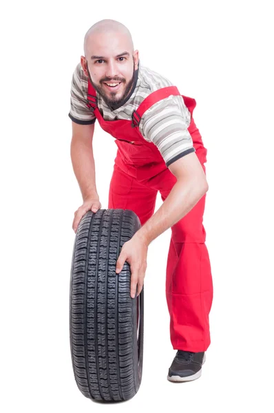 Lykkelig mekaniker skubber og ruller et bilhjul - Stock-foto