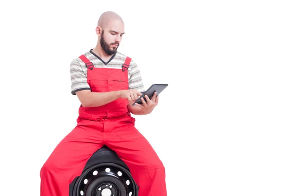 Mechanik za pomocą bezprzewodowej tabletka siedzi na koła samochodu — Zdjęcie stockowe