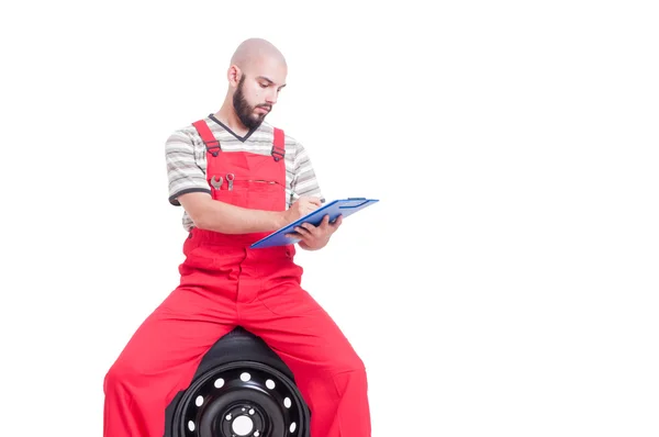 Mechanic schrijven op Klembord zittend op auto wielen — Stockfoto