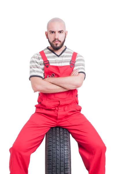 Joven mecánico con cara seria sentado en la rueda del coche — Foto de Stock