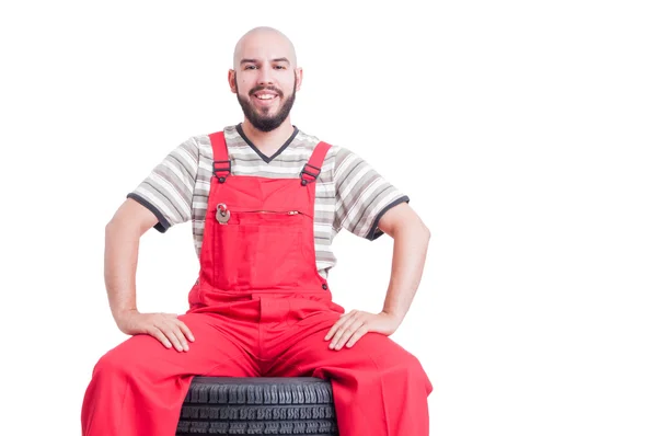 Feliz sorrindo mecânico sentado na pilha de rodas do carro — Fotografia de Stock