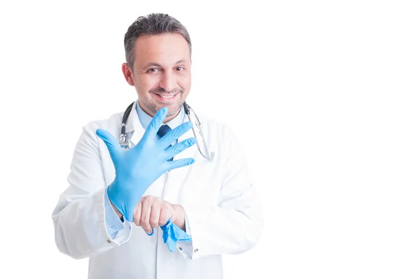 Przyjazny uśmiechający się lekarz lub lekarz ciągnąc niebieskie rękawice lateksowe — Zdjęcie stockowe
