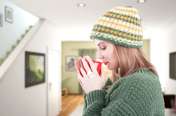 Cold woman wearing warm clothes and drinking tea at home