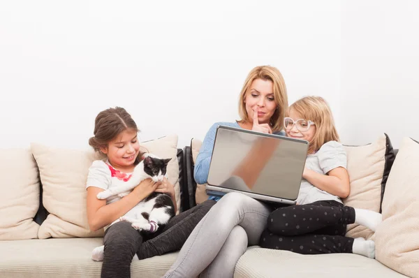 Madre e figlie utilizzando il computer portatile e giocando con il gatto — Foto Stock