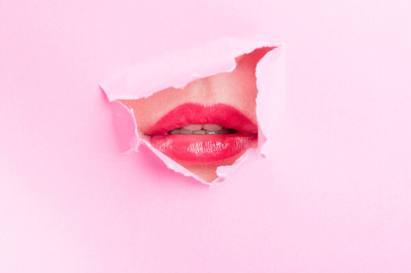 Cute woman mouth wearing red gloss thru ripped paper hole