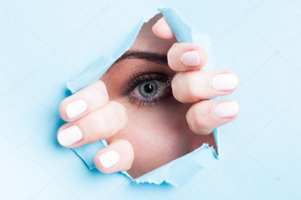 Woman blue eye with mascara looking thru ripped board