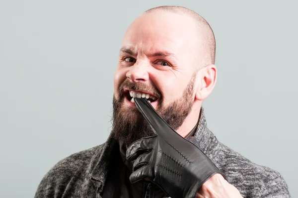 Angry bearded male biting his black glove — Stock Photo, Image